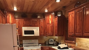 A kitchen with wooden cabinets, a white refrigerator, a microwave, an oven, and a sink. - Ticket to the great outdoors! (Heavener)