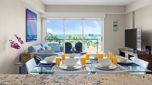 A dining area with a table set for breakfast, a sofa, and a TV in the background. - RELAXING and classic best BEACHFRONT condo. (Noord)