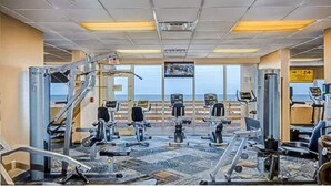 Un gimnasio con diversas máquinas de ejercicio, un amplio ventanal con vistas y un proyector instalado en el techo.