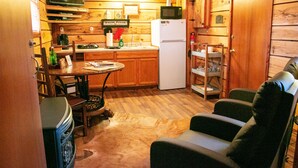 A compact kitchen with wooden cabinets, a refrigerator, a microwave, and a dining area with a table and chairs. - The Cabin at Panther Valley Ranch (Hot Springs)