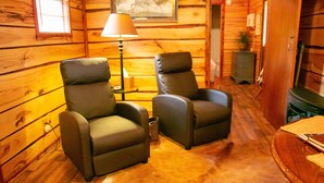 A cozy cabin interior with two leather armchairs, a wooden floor, a lamp, and a fireplace. - The Cabin at Panther Valley Ranch (Hot Springs)