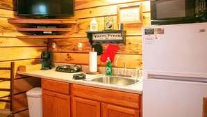 A compact kitchen with wooden cabinets, a stainless steel sink, a microwave, and a refrigerator. - The Cabin at Panther Valley Ranch (Hot Springs)