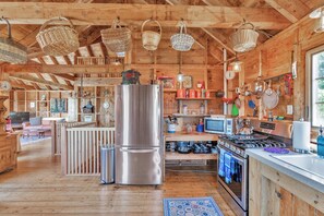 A rustic cabin interior with a wooden interior, a stainless steel refrigerator, a kitchen area with a stove, and hanging baskets.
