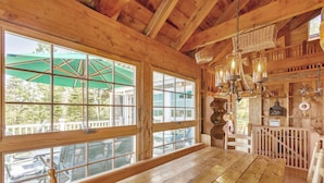 A wooden interior with large windows, a wooden table, and a hanging light fixture. - Sunset House: Rustic Maine Cottage Perched High Above Fishing Village with Harbor Views (Port Clyde)