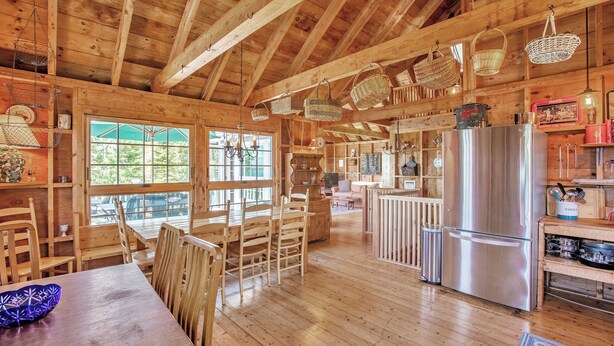 A wooden cabin interior with a dining area, kitchen, and large windows. - Sunset House: Rustic Maine Cottage Perched High Above Fishing Village with Harbor Views (Port Clyde)
