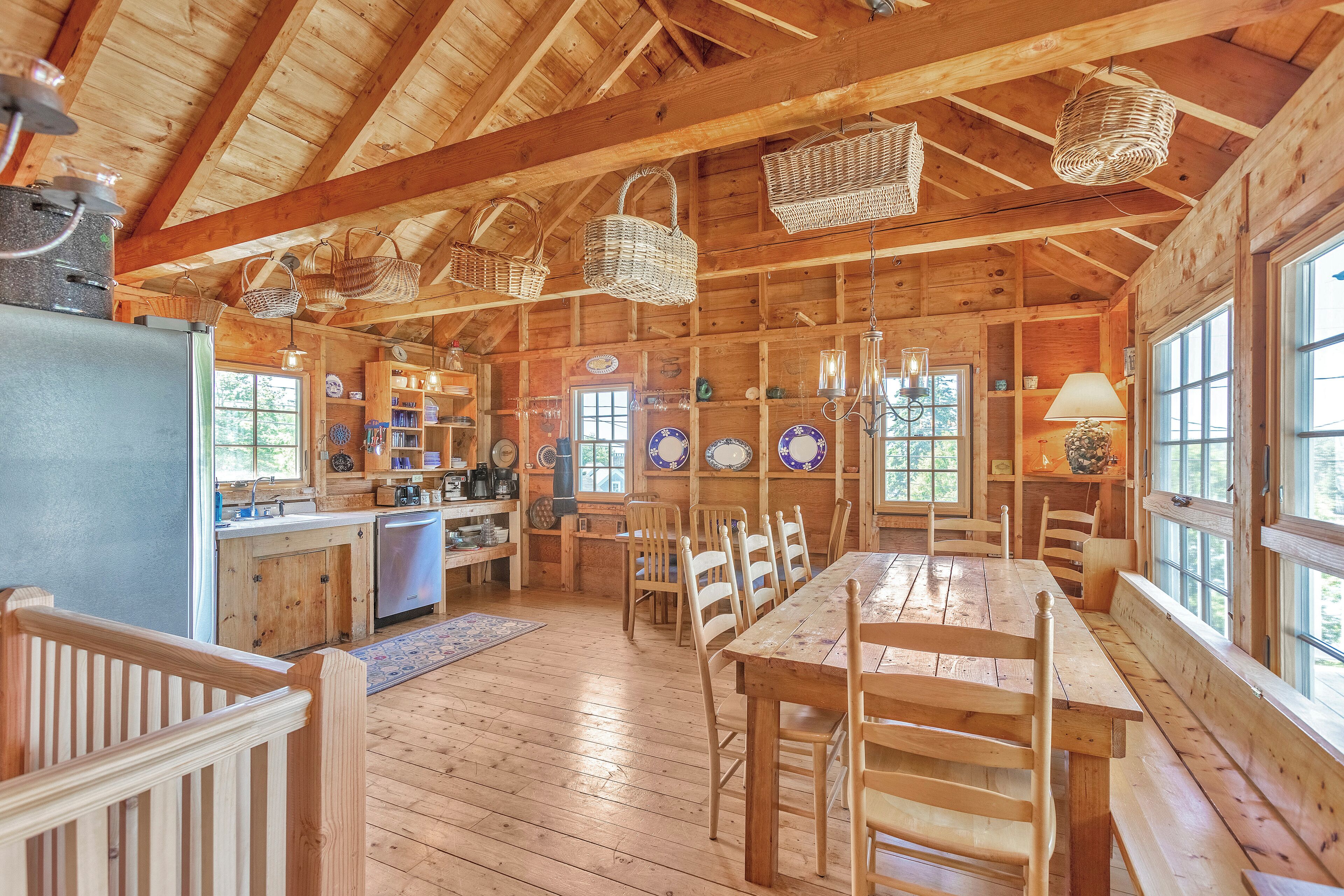 A rustic wooden cabin interior with a dining area, kitchen, and large windows.