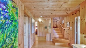 A wooden interior with a staircase, wooden walls, and a large abstract painting. - Sunset House: Rustic Maine Cottage Perched High Above Fishing Village with Harbor Views (Port Clyde)