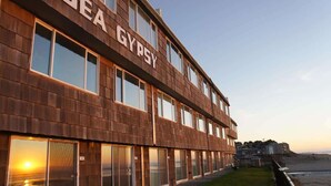 A multi-story building with the name "SEA GYPSY" on the facade, large windows, and a view of the beach.