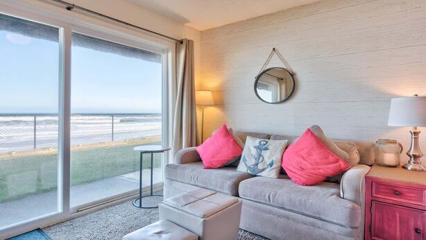 A modern room with a grey sofa, pink and blue cushions, a round mirror, and a lamp.