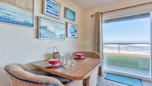 A dining area with a wooden table, chairs, and a view of the ocean through a large window.
