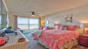 A bedroom with a large bed, a desk, a chair, and a view of the beach.