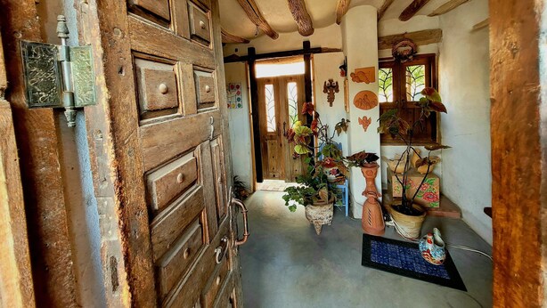 Un corridoio rustico con porte in legno, pavimento piastrellato e diversi oggetti decorativi, tra cui piante e ceramiche.