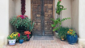 Una porta in legno decorata con una ghirlanda floreale, affiancata da vasi con piante e un numero esposto a parete.