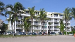 Un hôtel à plusieurs étages, doté de balcons, entouré de palmiers et bordé de voitures garées.