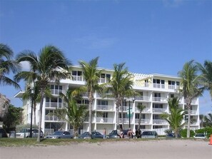 A multi-story hotel with balconies, surrounded by palm trees and parked cars. - Direct Oceanfront Luxury, Beautifully Redone! Satisfaction Guaranteed (Deerfield Beach)