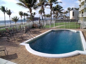 A rectangular pool with a white edge, surrounded by lounge chairs and a white fence. - Direct Oceanfront Luxury, Beautifully Redone! Satisfaction Guaranteed (Deerfield Beach)