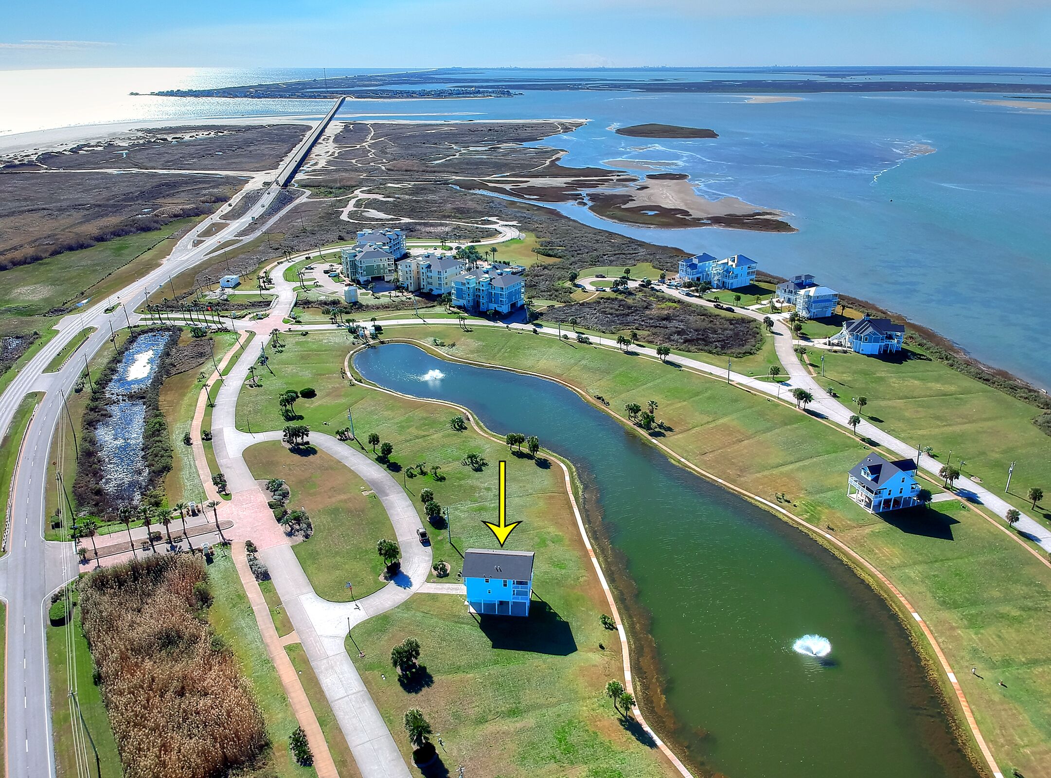 An aerial view of a coastal residential area with a golf course, a marina, and several blue houses.