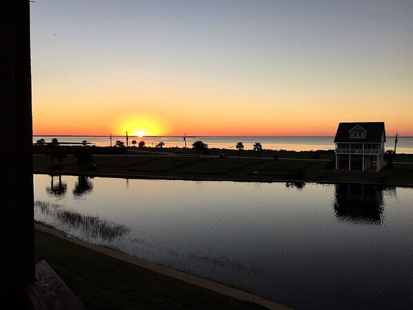 Uma casa perto de águas calmas com o pôr do sol ao fundo.