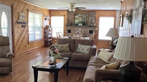A spacious living room with wooden flooring, a sofa, a coffee table, and a dining area with a stone fireplace.