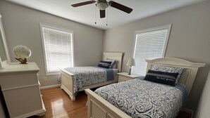 A bedroom with two beds, a dresser, and a ceiling fan.