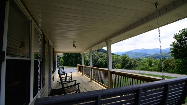 A covered porch with a wooden bench, a swing, and a view of mountains.