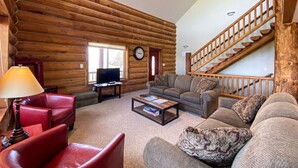 L’intérieur d’une cabane en rondins comprend un salon, un fauteuil rouge, un téléviseur, une table basse et un escalier.