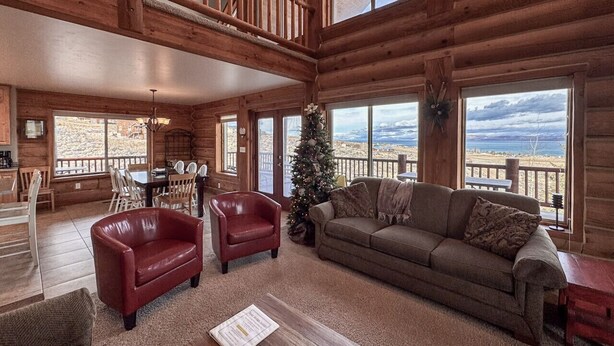 Un intérieur spacieux de chalet en bois, avec un plafond haut, un coin salon confortable et une vue sur l’extérieur.