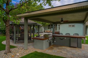 A covered outdoor kitchen area with a grill, seating, and a pergola structure.
