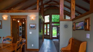 A spacious interior with wooden beams, a dining area with chairs, a kitchen, and a view through a glass door to the outdoors.