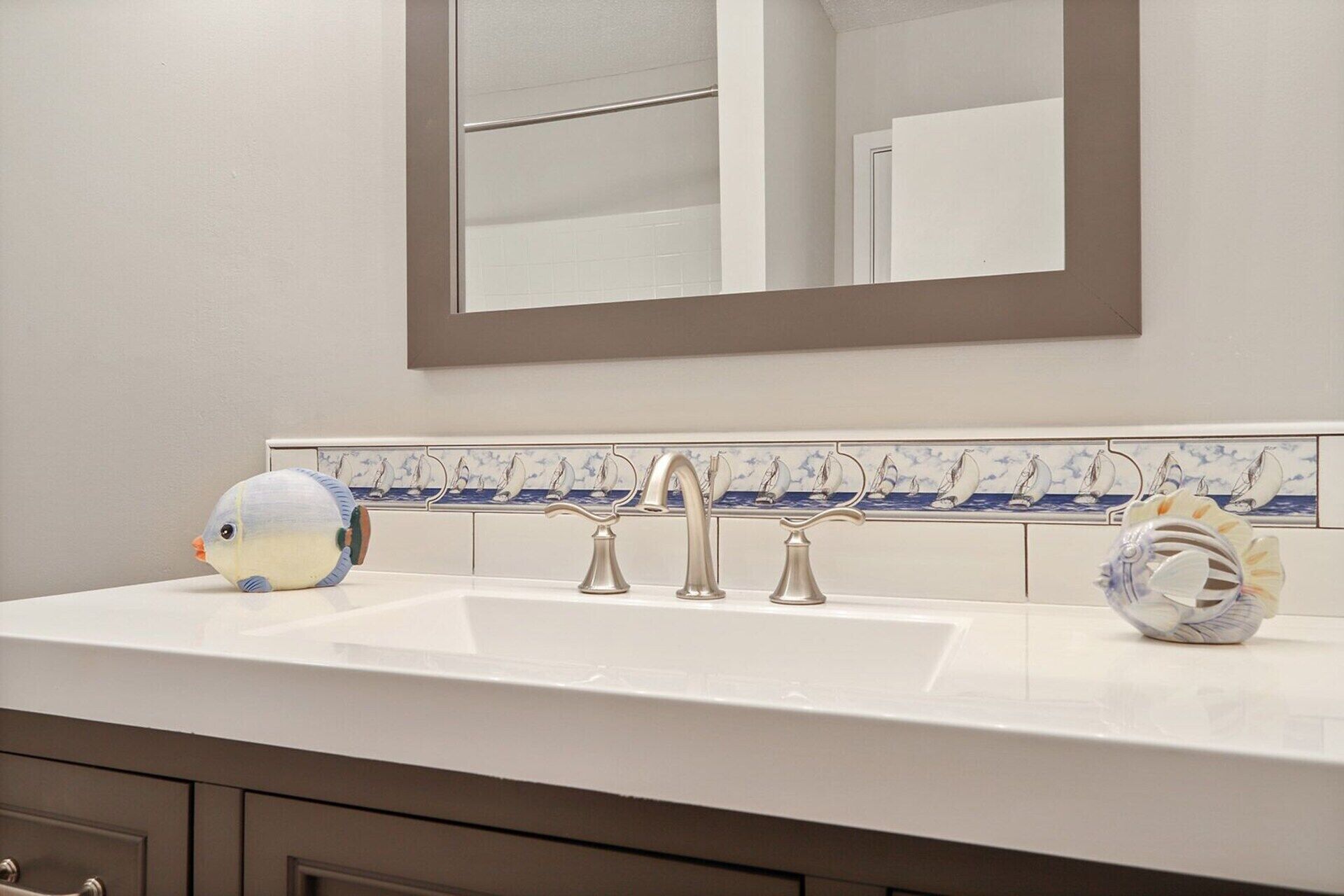 A bathroom with a white sink, three faucets, a mirror, and a tiled backsplash with sailboat designs.