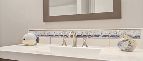 A bathroom with a white sink, three faucets, a mirror, and a tiled backsplash with sailboat designs.