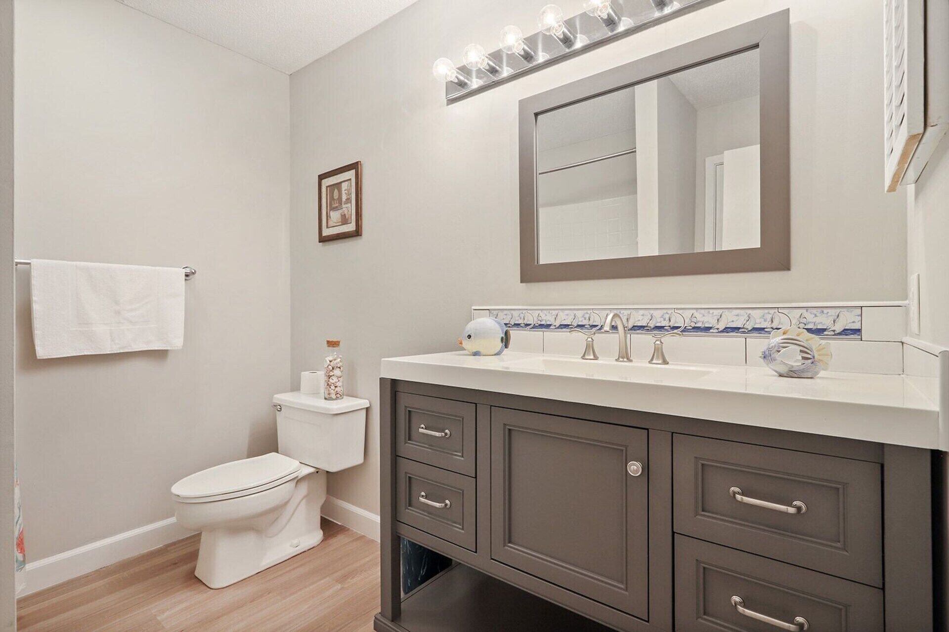 Une salle de bain comprenant des toilettes, un meuble-lavabo avec des tiroirs, un miroir et un porte-serviettes.