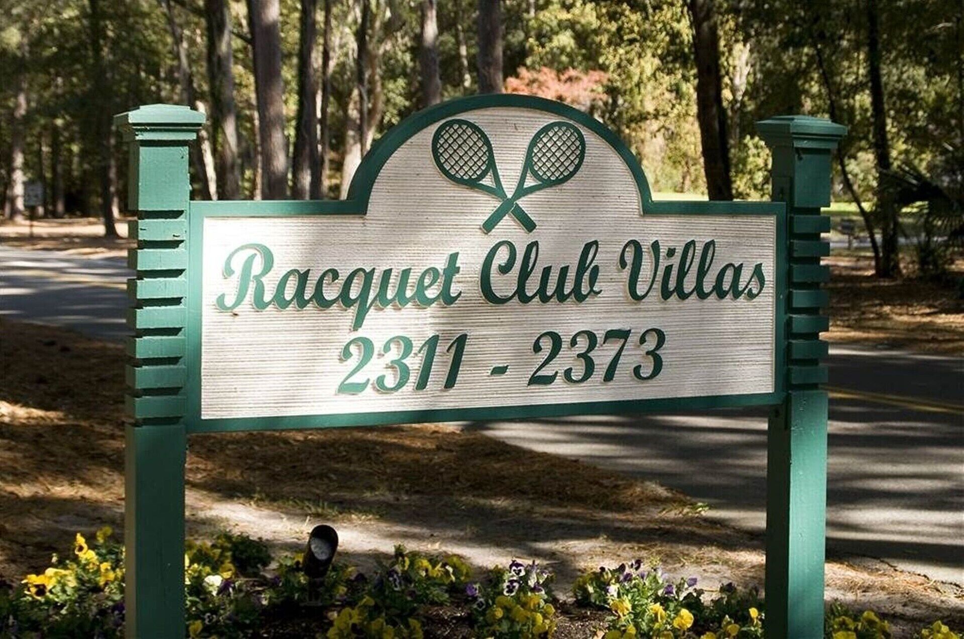 A sign for Racquet Club Villas with a tennis racket design, listing the address 2311-2373.