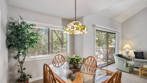A dining area with a glass table, wicker chairs, a hanging light fixture, and a large potted plant. - Harbour Town Gem: Serene Lagoon Views & Steps to the Lighthouse (Hilton Head Island)