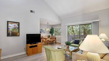 A living room with a TV, a dining area with chairs, a sofa, and a lamp.