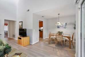 A modern living room with a TV, dining area with chairs, and a kitchen in the background. - Harbour Town Gem: Serene Lagoon Views & Steps to the Lighthouse (Hilton Head Island)