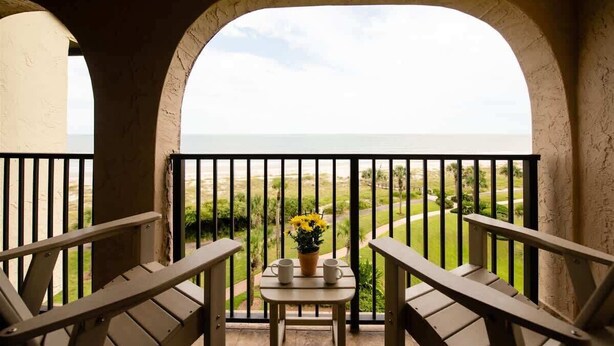 Un balcon donnant sur la mer, une table avec deux tasses et un vase rempli de fleurs jaunes.