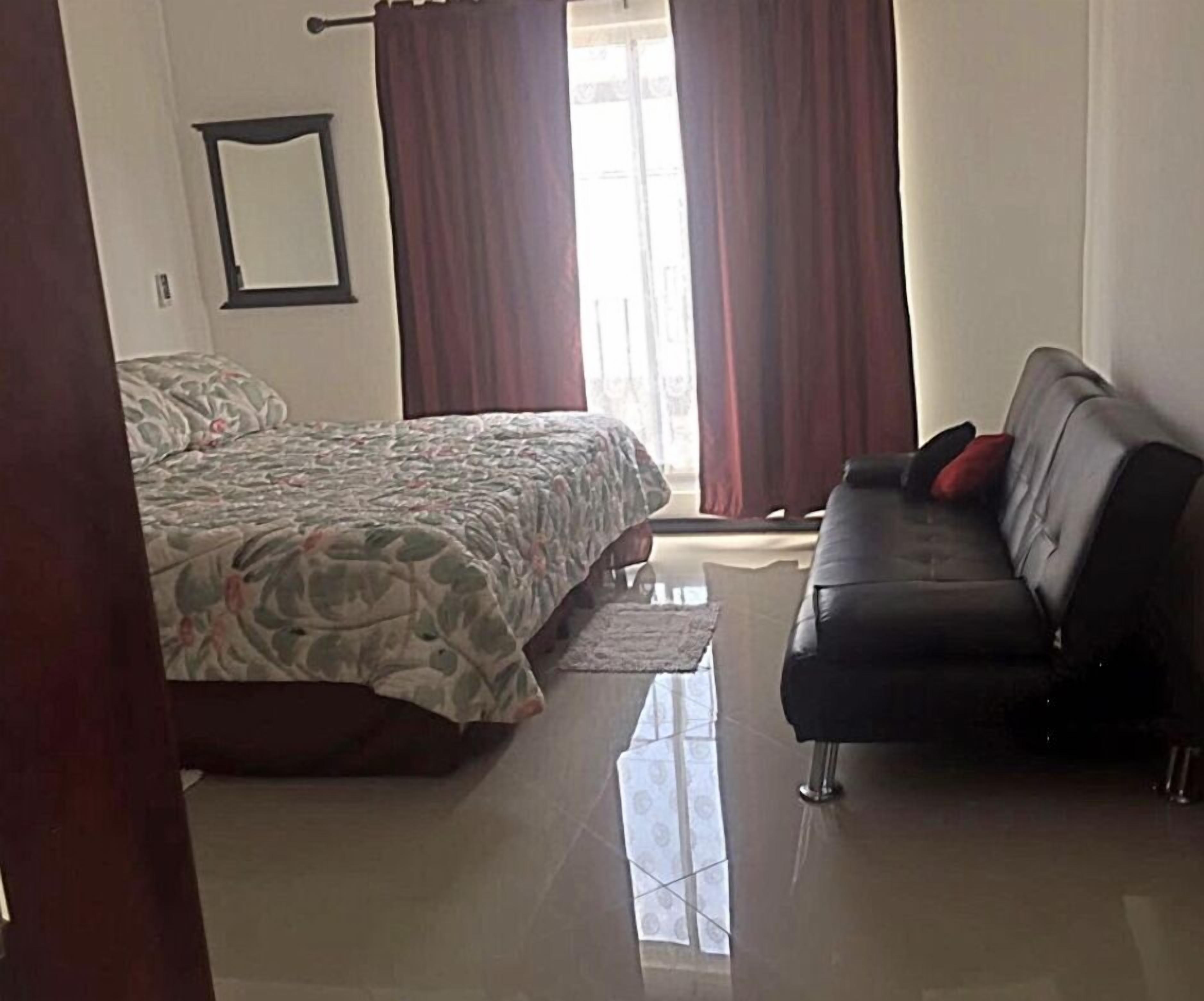 Un dormitorio con cama, sofá y ventana con cortinas.