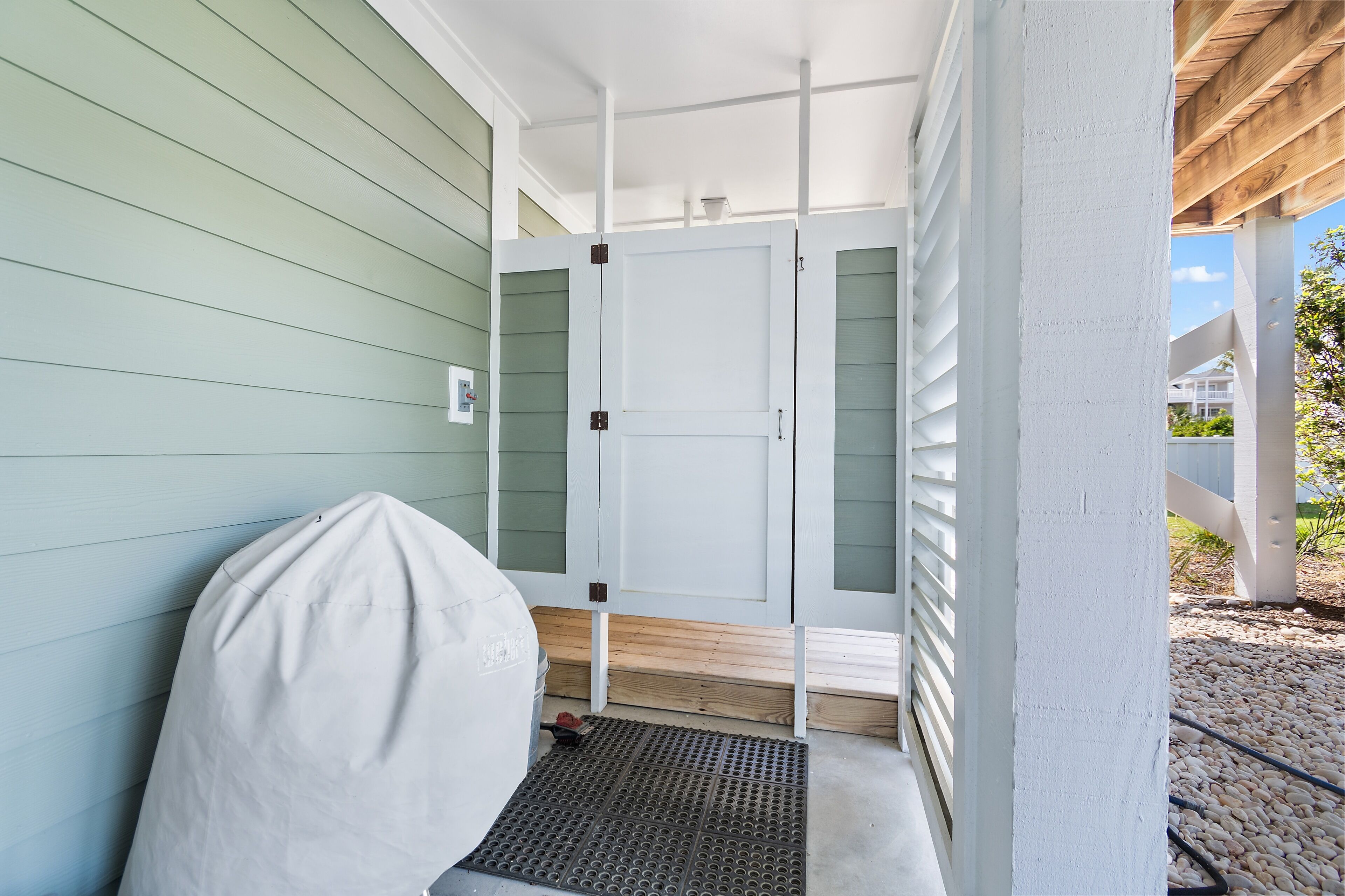 A covered porch with a white door, a covered grill, and a wooden bench.