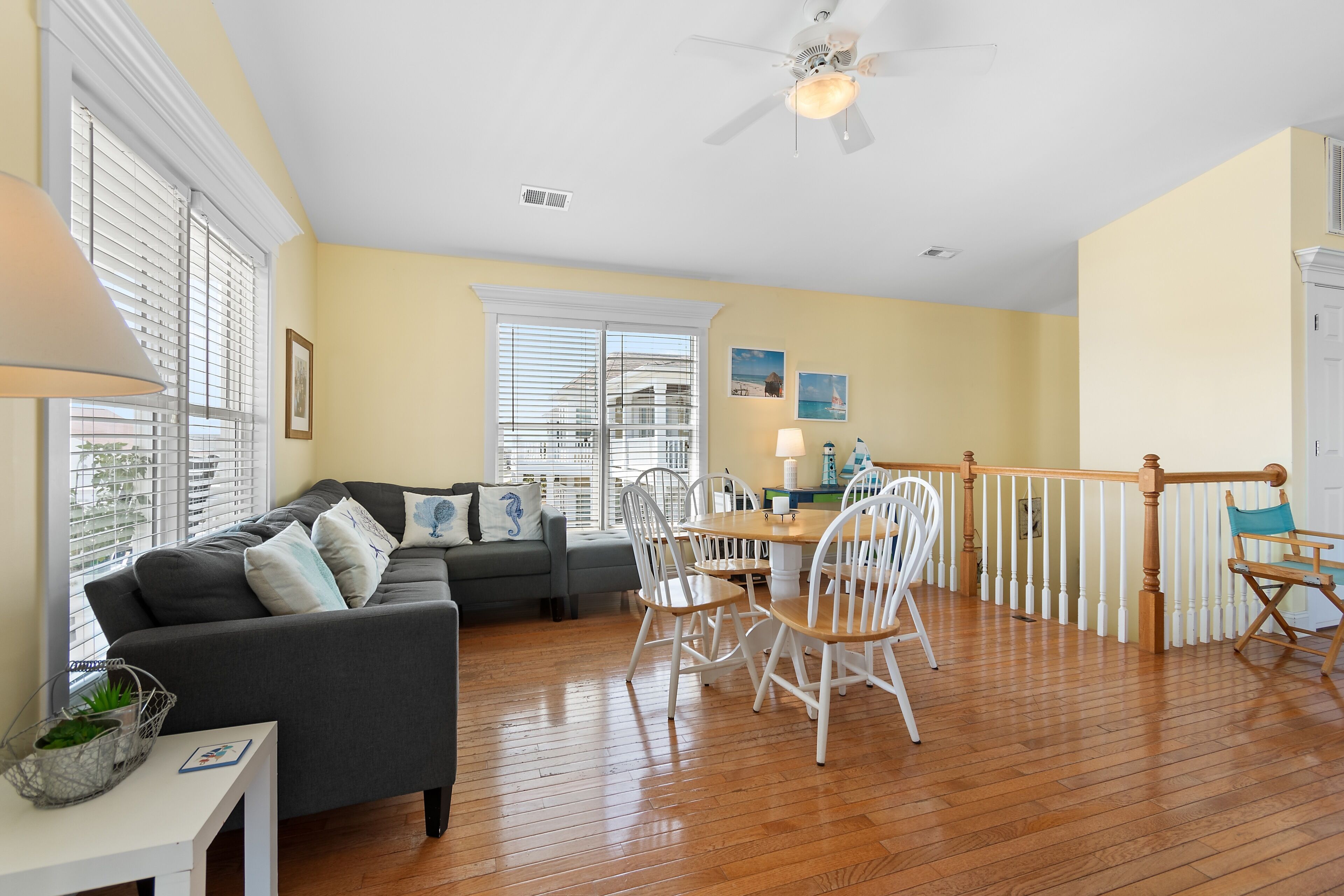 A spacious living area with a wooden floor, a grey sofa, white chairs, and a dining table.