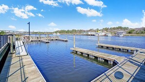 Un puerto deportivo con muelles de madera y barcos, un puente al fondo y un cielo despejado.