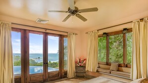 Ein Schlafzimmer mit einem großen Bett, einem Deckenventilator und Meerblick durch große Schiebetüren.