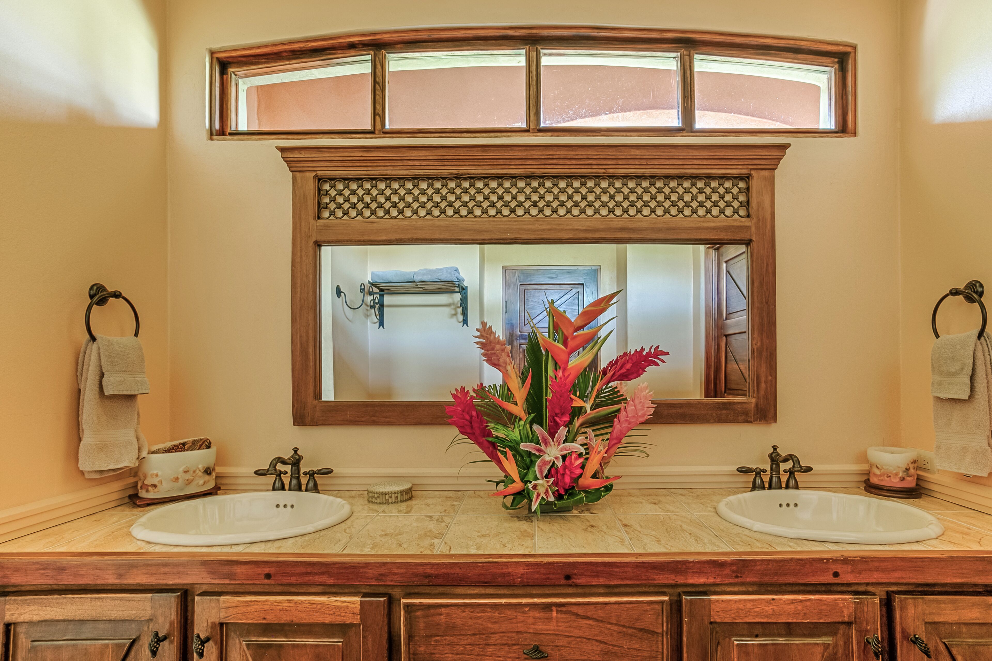 Un baño con dos lavamanos, un mueble de tocador de madera, un espejo con marco decorativo y una ventana sobre el espejo.