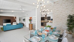 A modern dining area with a glass table set for six, surrounded by white chairs.