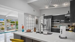 A modern kitchen with a white countertop, stainless steel appliances, and yellow bar stools.