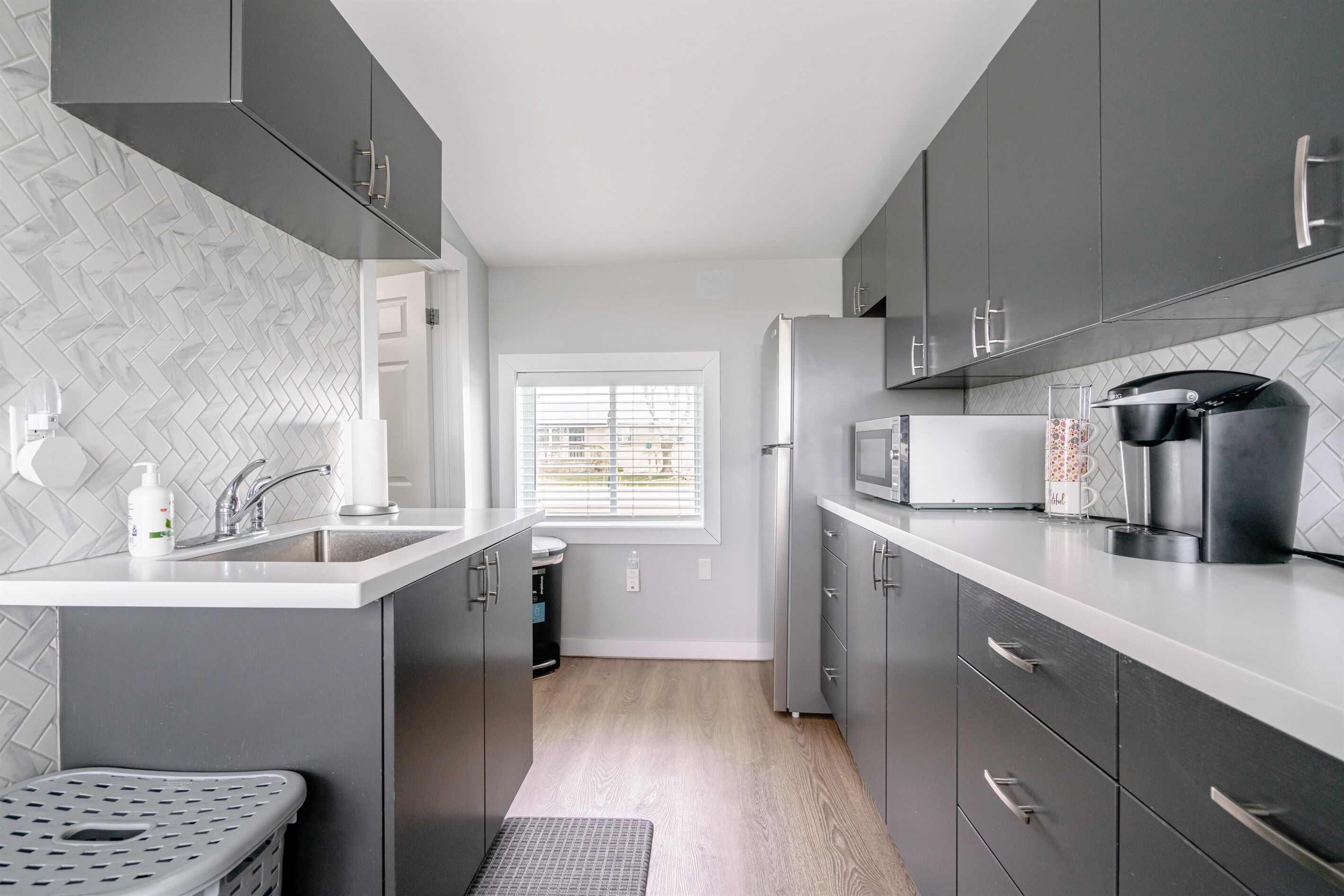 A modern kitchen with grey cabinets, a white countertop, a built-in microwave, and a coffee machine.