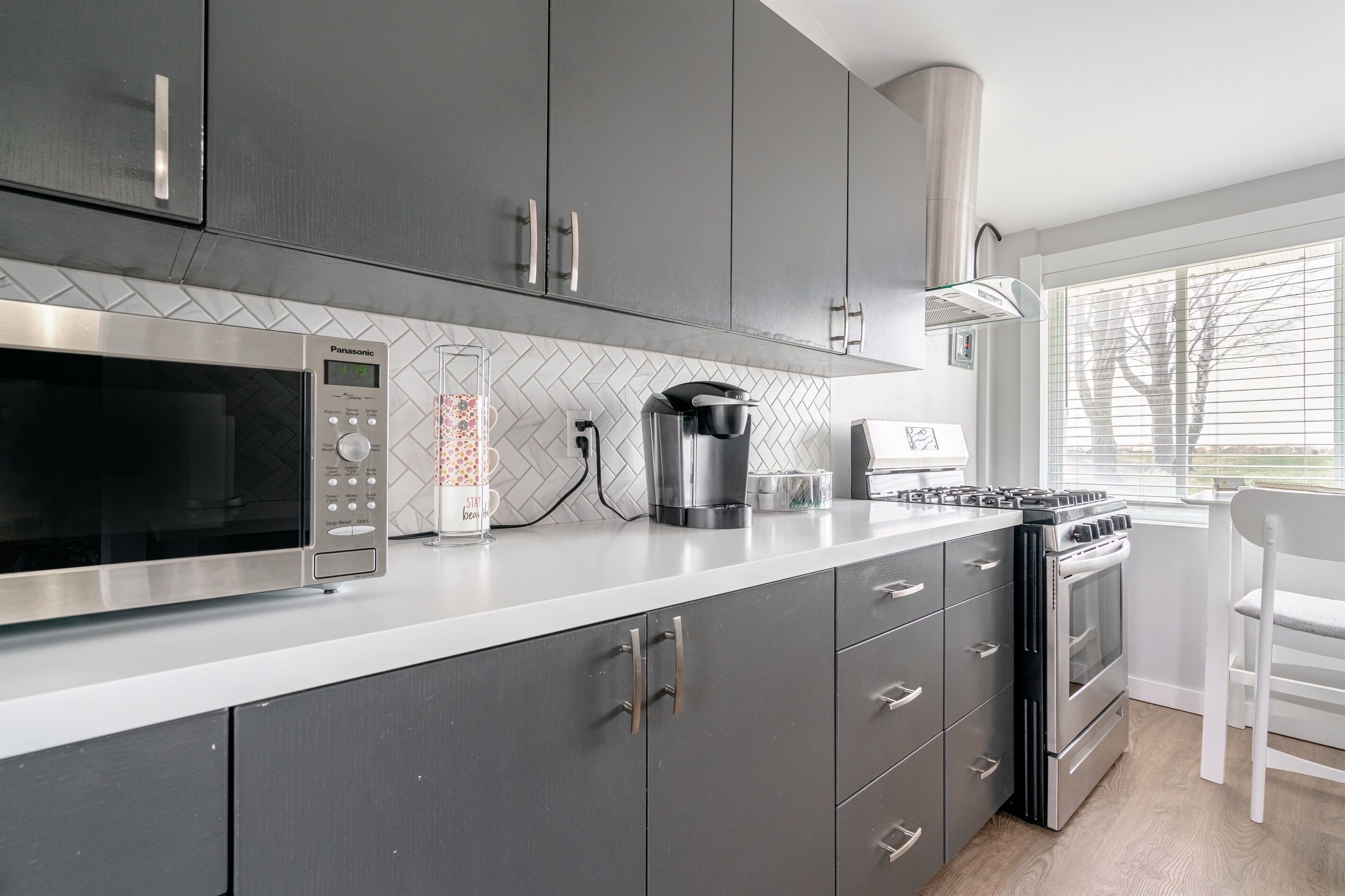 A modern kitchen with grey cabinets, a stainless steel microwave, a coffee maker, and a gas stove.
