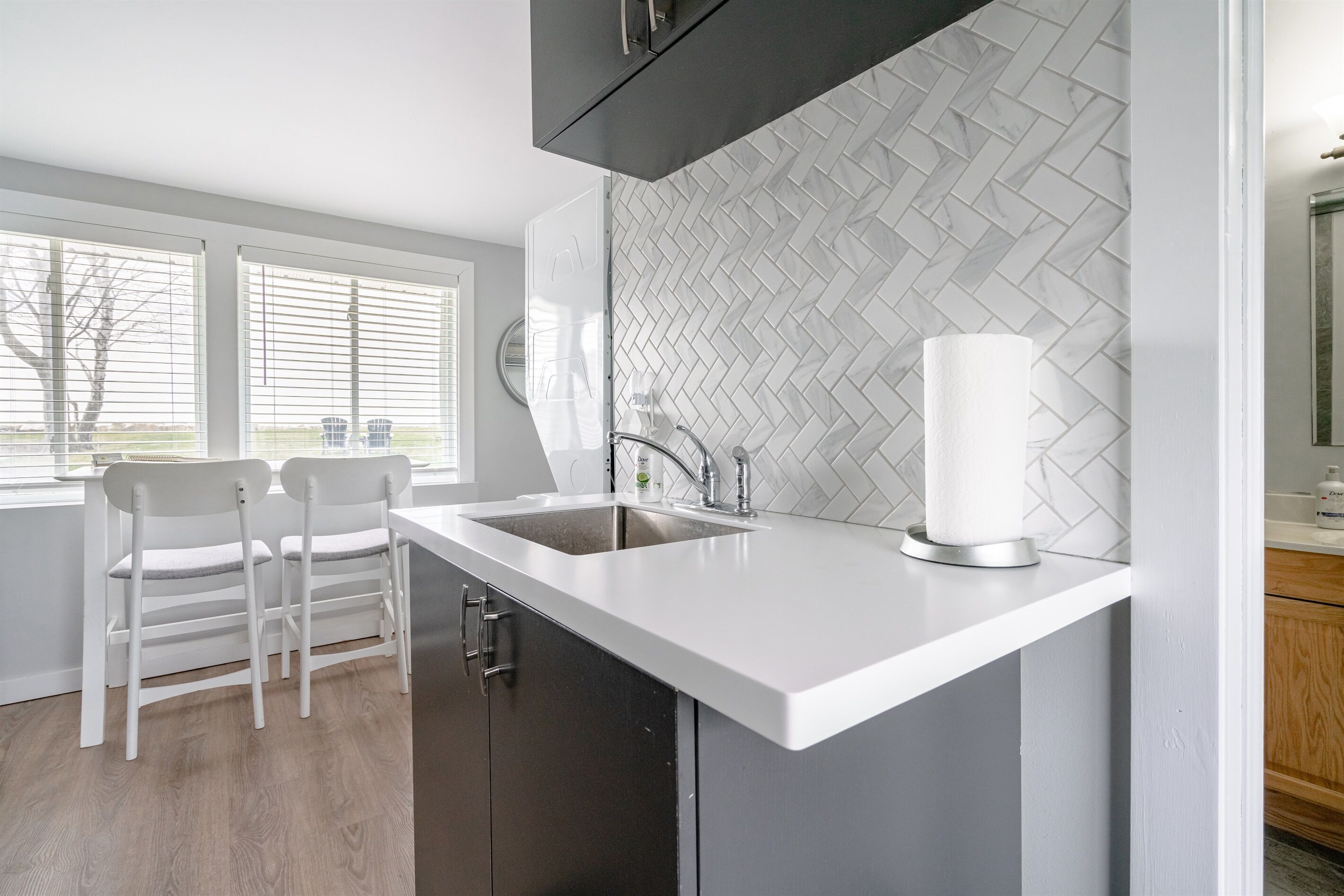 A modern kitchen with a white countertop, two white chairs, a sink, and a herringbone-patterned backsplash.