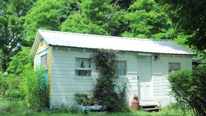 A small, single-story house with a gabled roof, surrounded by lush greenery. - A cozy country "Doll House," with everything to meet your needs. (Hector)