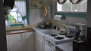 A kitchen with a stove, oven, and a toaster. There is a window with curtains and a plant outside. - A cozy country "Doll House," with everything to meet your needs. (Hector)